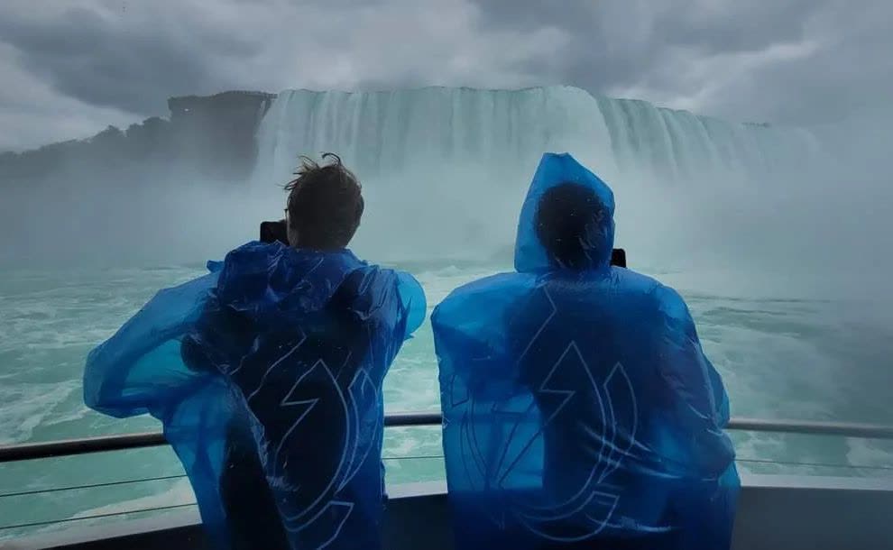 Two visitors in blue ponchos facing Horseshoe Falls from the deck of the Maid of the Mist boat tour