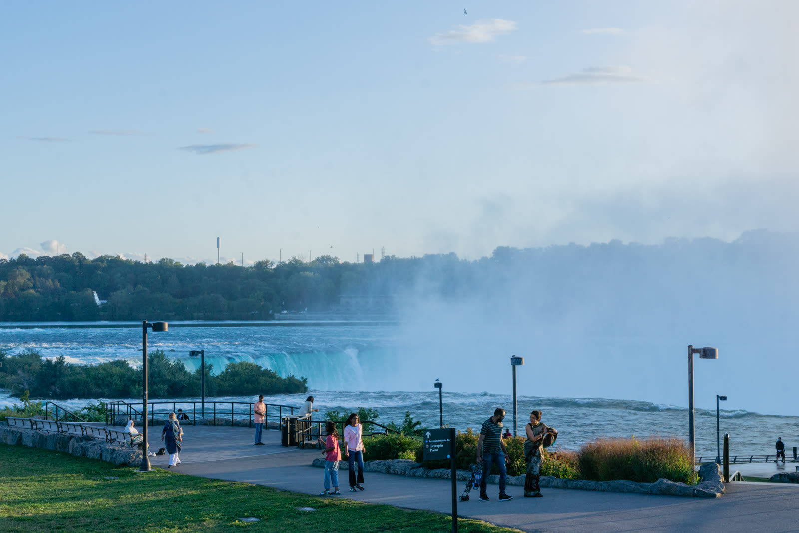 Families walking the Terrapin Point path at golden hour with Horseshoe Falls and mist behind, Niagara Falls State Park